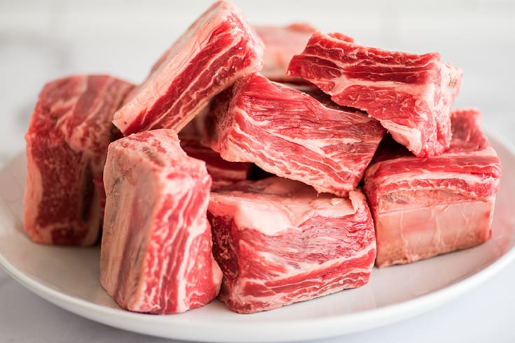 Meat delivery Dubai: Fresh, tender raw meat cuts on a wooden board, ready for cooking, with herbs and spices on the side."