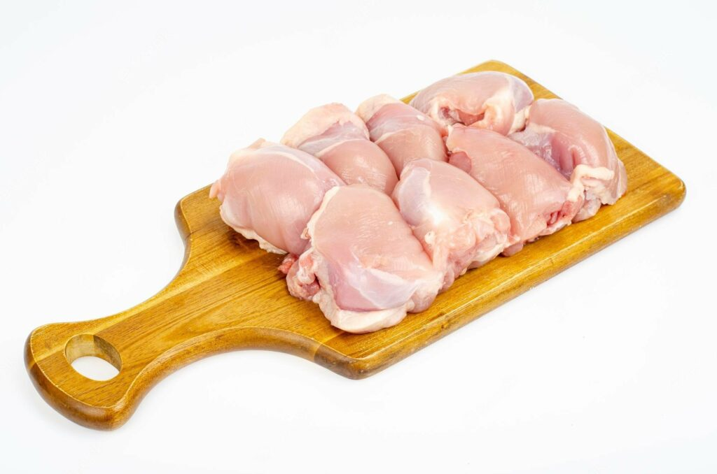 Meat delivery Dubai: Fresh, tender raw meat cuts on a wooden board, ready for cooking, with herbs and spices on the side.